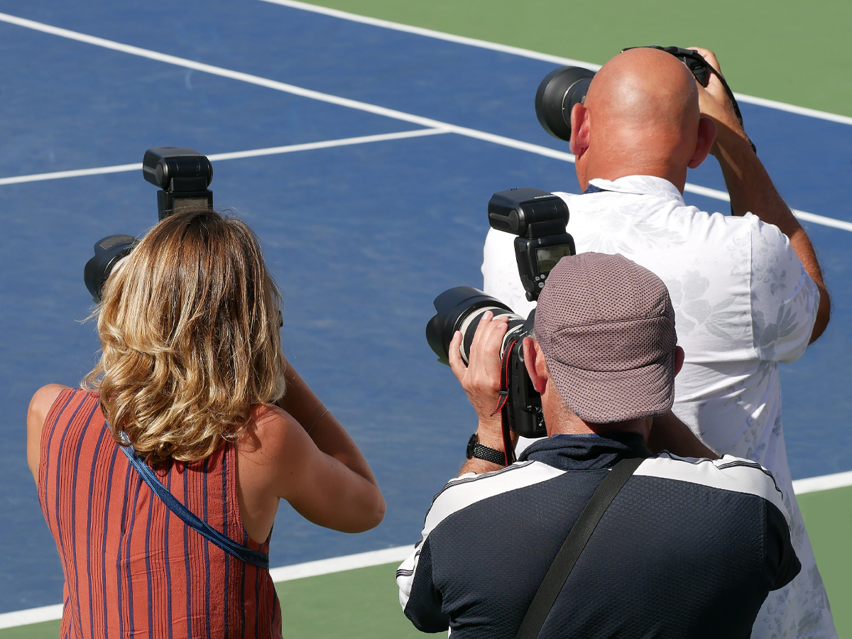 Group of photographers taking photos on a tennis court.